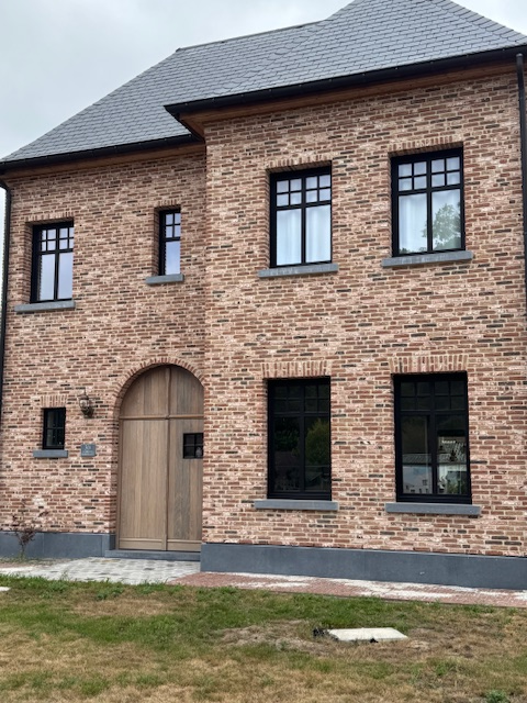 Voorkant van landelijk huis met zwarte aluminium ramen en een grote houten deur